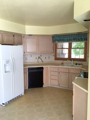 Dated kitchen with soffits, mismatched white and black appliances, lighter wood cabinets, and linoleum flooring.
